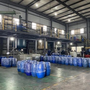 Industrial warehouse with blue barrels and workers operating machinery.