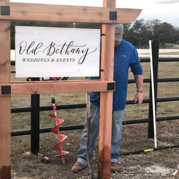 Wooden Structure with metal sign & man working to drill a large hole in the ground for installation.