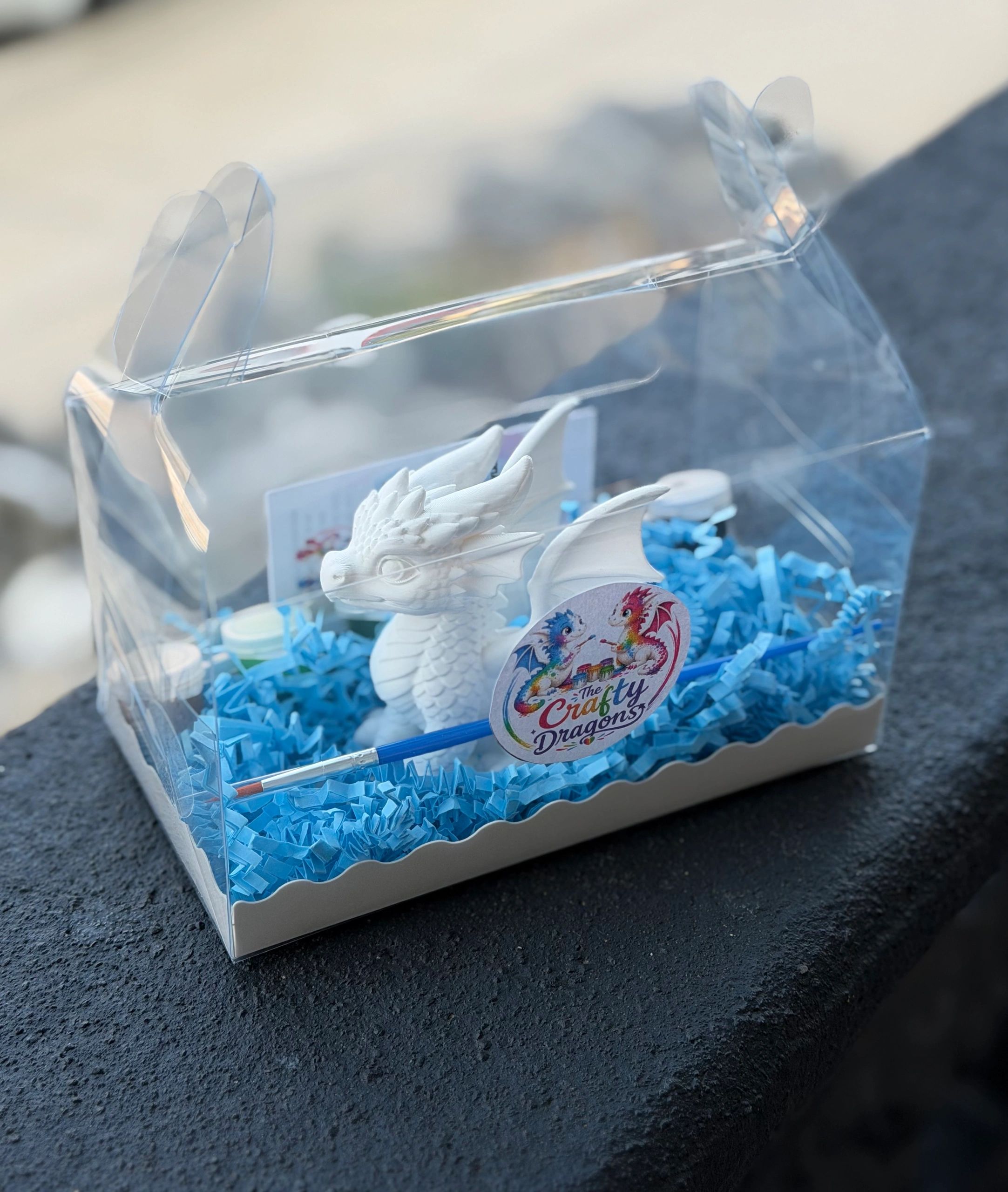 Unpainted dragon figure kit in packaging with blue shredded paper and paintbrush.