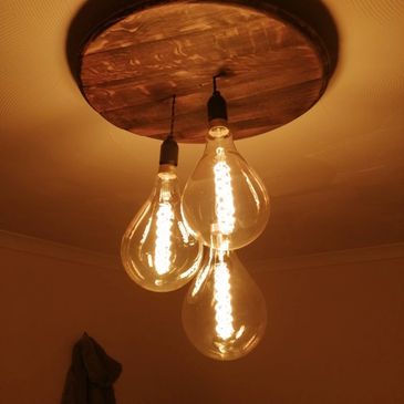 Three vintage-style light bulbs hanging from a wooden ceiling fixture.