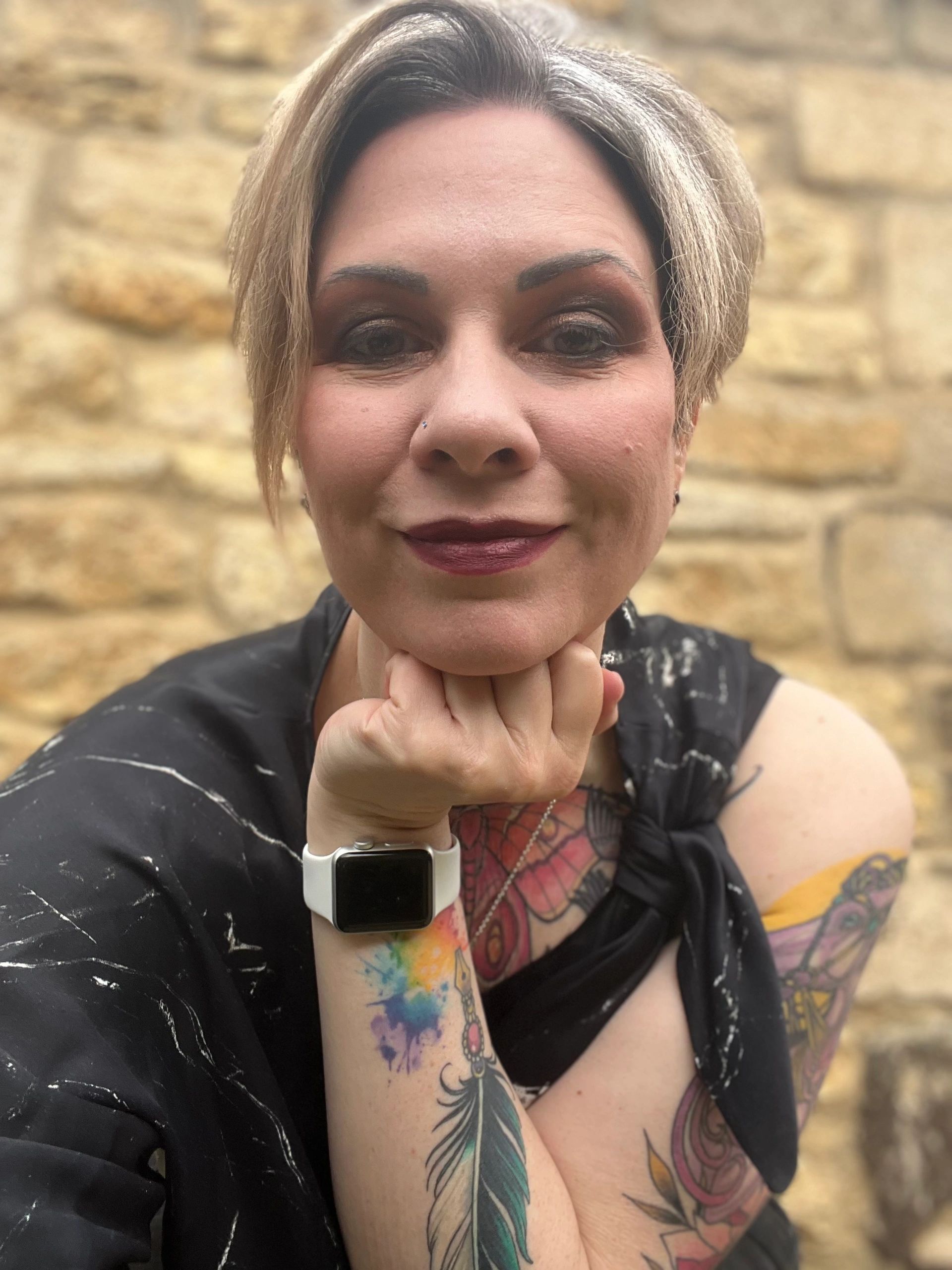 A smiling woman with short hair and tattoos. Writer Maddy T Thomas. 