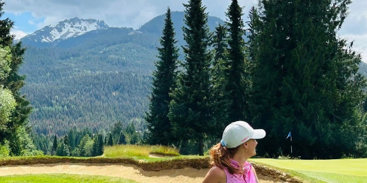 Woman in pink golf attire standing on a lush golf course with mountainous backdrop.