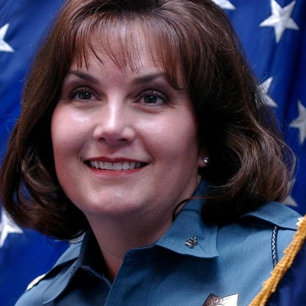 Smiling female police officer in uniform with American flag backdrop.