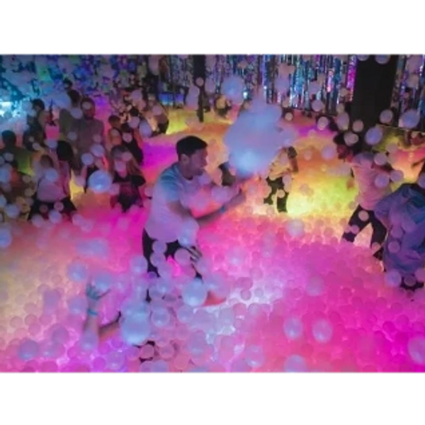People enjoying a colorful ball pit with vibrant lighting at an indoor event.