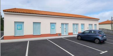 A single-story building with blue windows and a parked car outside.