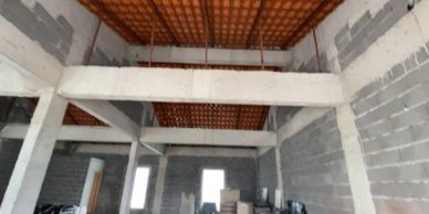 An unfinished room with concrete columns and scattered furniture.