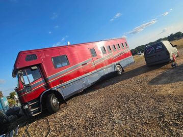Red and silver RV parked on gravel under blue sky.