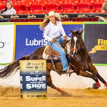 A rider in cowboy attire racing a horse around a barrel indoors.