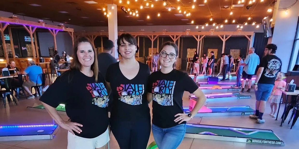 Three women posing at an indoor mini golf venue.