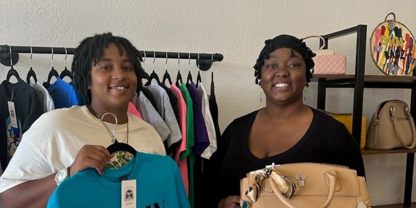 Two women smiling in a clothing and accessories store.