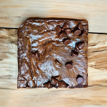 Square chocolate brownie with chocolate chips on wooden surface.