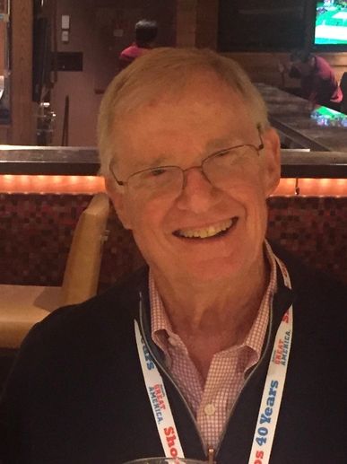 Elderly man with glasses smiling warmly in a restaurant setting.