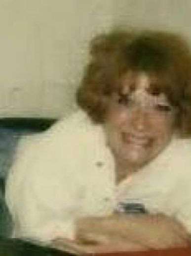 Smiling woman with curly hair leaning forward indoors.