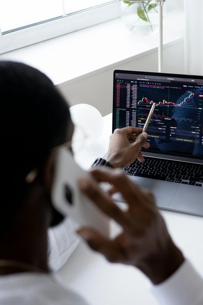 Person analyzing stock charts on laptop while talking on phone.