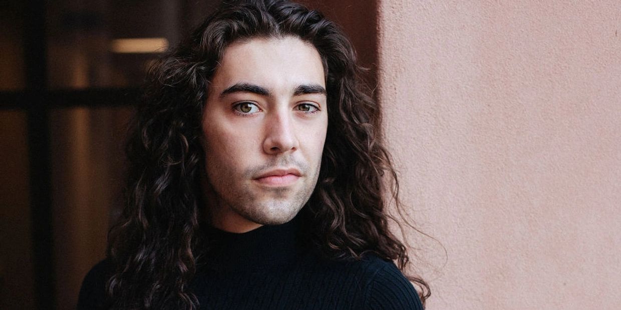 Portrait of a man with long curly hair and green eyes.