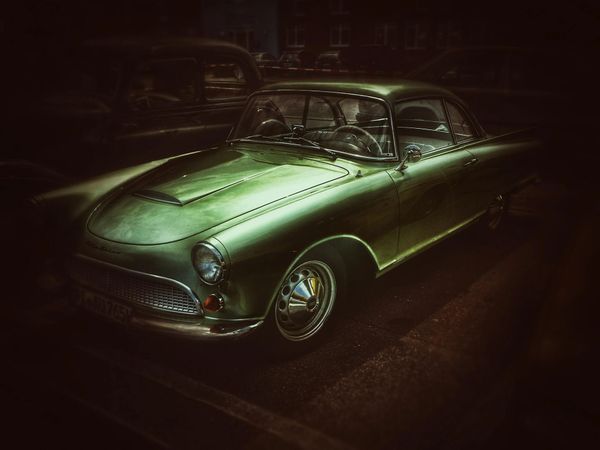 A classic green vintage car parked in a dimly lit street.