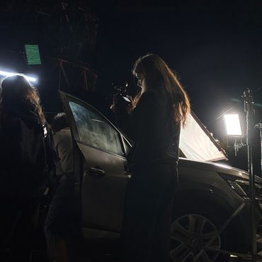 People filming or photographing near a car at night with bright lights.