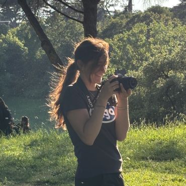 A woman with a ponytail takes photos outdoors on a sunny day.
