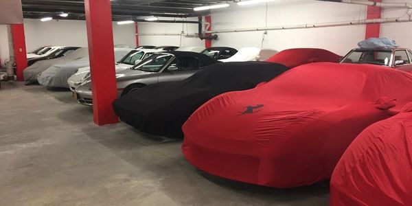 Stored vehicles covered in car covers sitting in large garage with red pillars