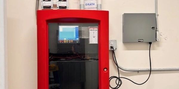 Red fire alarm control panel with digital display and connected equipment.