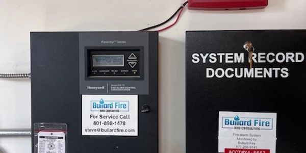 Fire safety control panels and system record documents mounted on a wall.