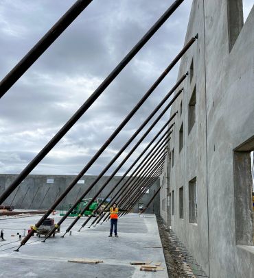 Construction worker standing beside reinforced concrete walls with diagonal support beams.