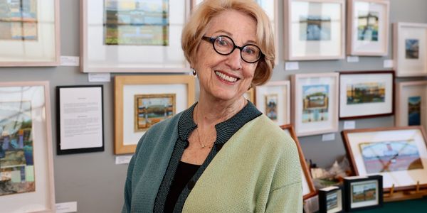 Smiling elderly woman with glasses in an art gallery.