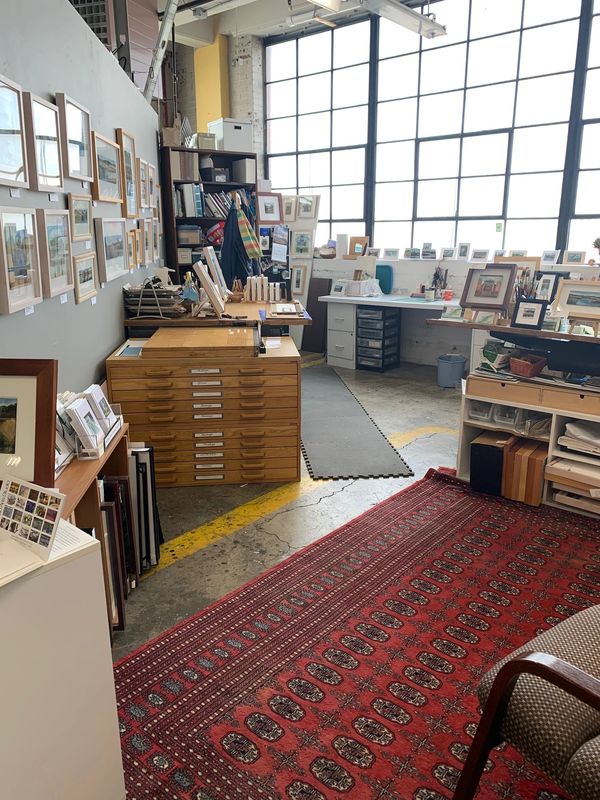 Art studio with framed pictures, wooden drawers, and a large window.