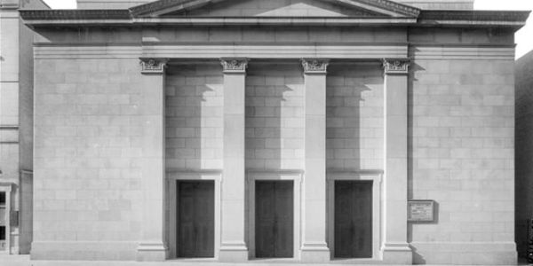 Black and white photo of a neoclassical building with three doors and columns.