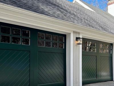 Two dark green garage doors on a white house.