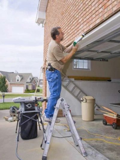 Man repairs garage door while standing on a ladder.