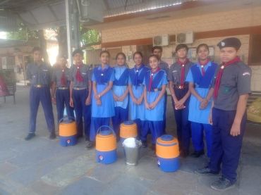 Group of school children in uniform standing with water coolers.
