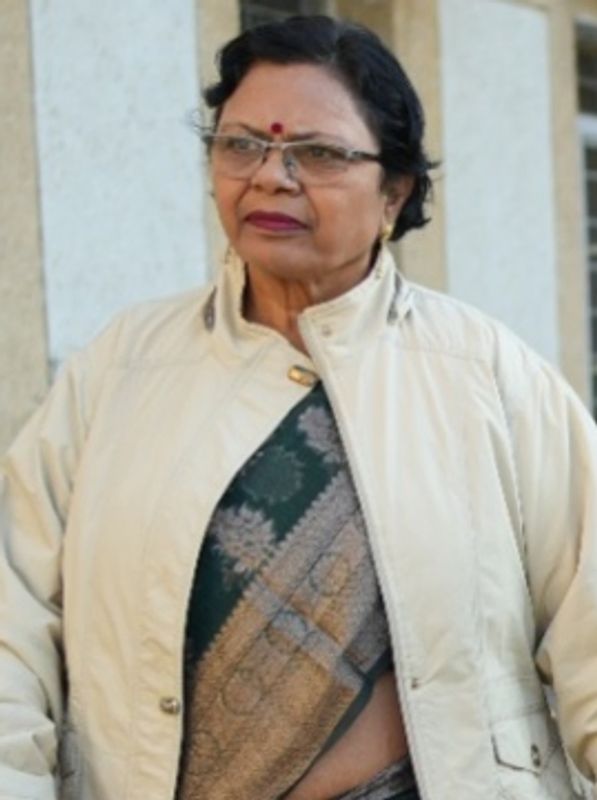 Elderly woman wearing glasses and a beige jacket over a traditional sari.