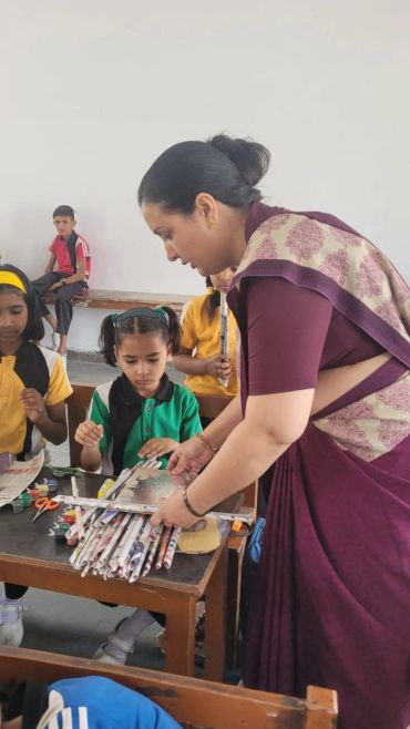 Teacher helping kids with craft project using rolled newspapers.