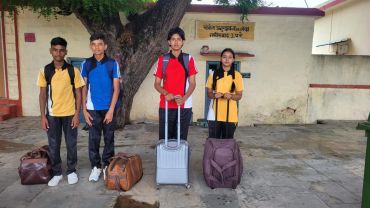 Four students with luggage standing outside a building.