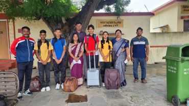 Group of students and teachers posing with luggage outdoors.