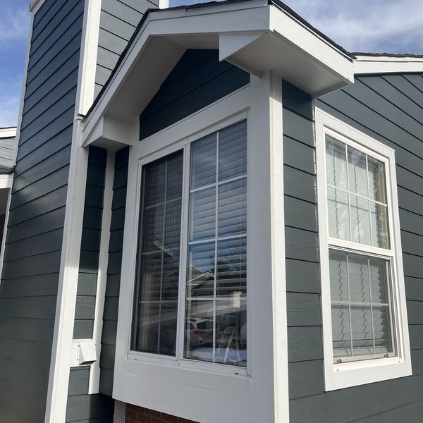A modern bay window with white trim on a gray house exterior. Showing Finished Siding job. 