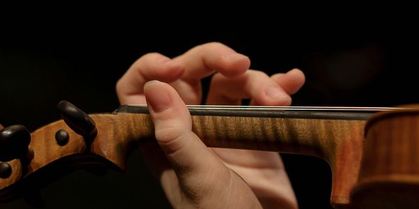 Close-up of fingers playing a violin on the fingerboard.