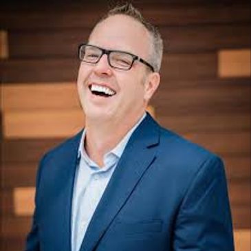 A man in glasses and a blue suit laughing joyfully.