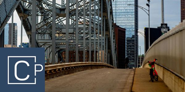 Steel bridge structure with cityscape and bike lane under cloudy sky.
