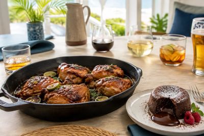 Glazed chicken thighs in a cast-iron skillet beside a molten chocolate cake on a bright coastal home