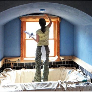 Plaster artist Bridey O'Brien reaches up to scrape a blue arched ceiling above a bathtub