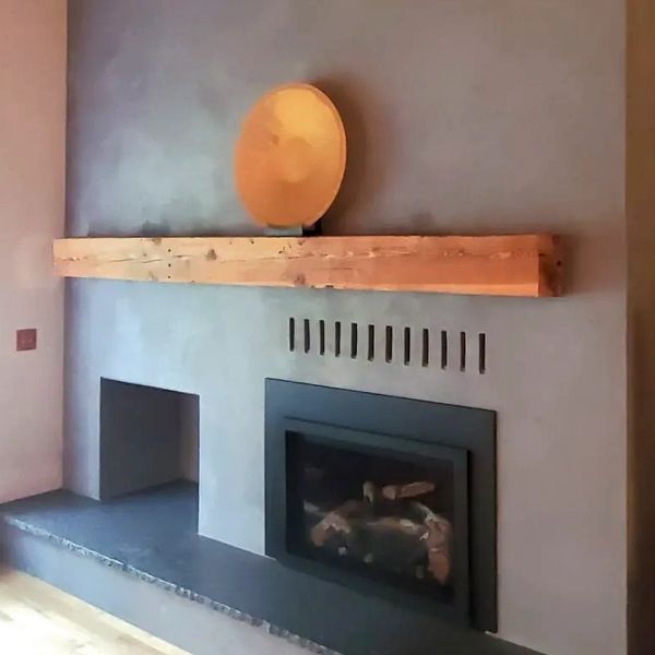 Floor-to-ceiling fireplace redone with grey-blue plaster. Mantle with a gold plate displayed.