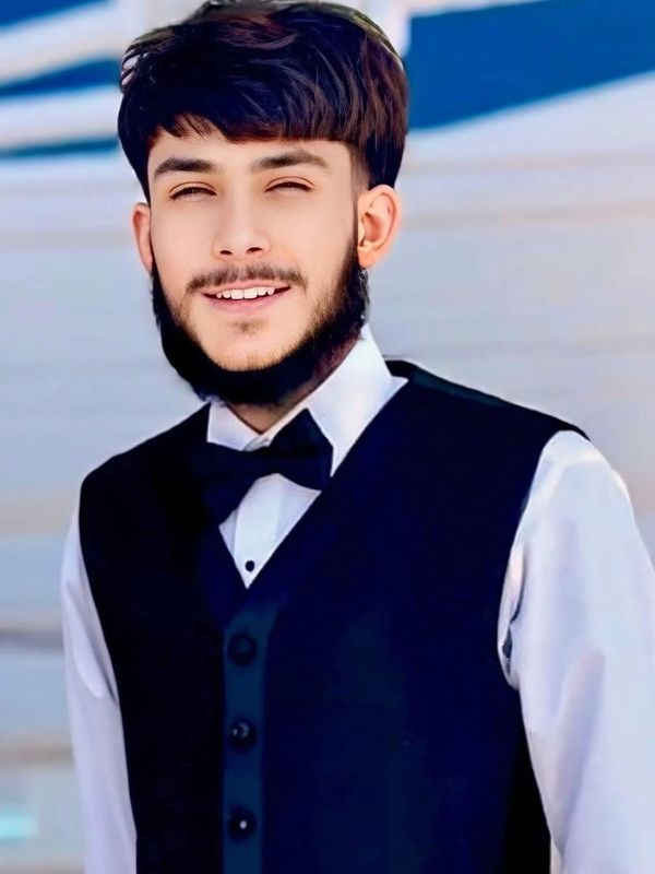 Young man smiling, dressed in a formal black vest and bow tie.