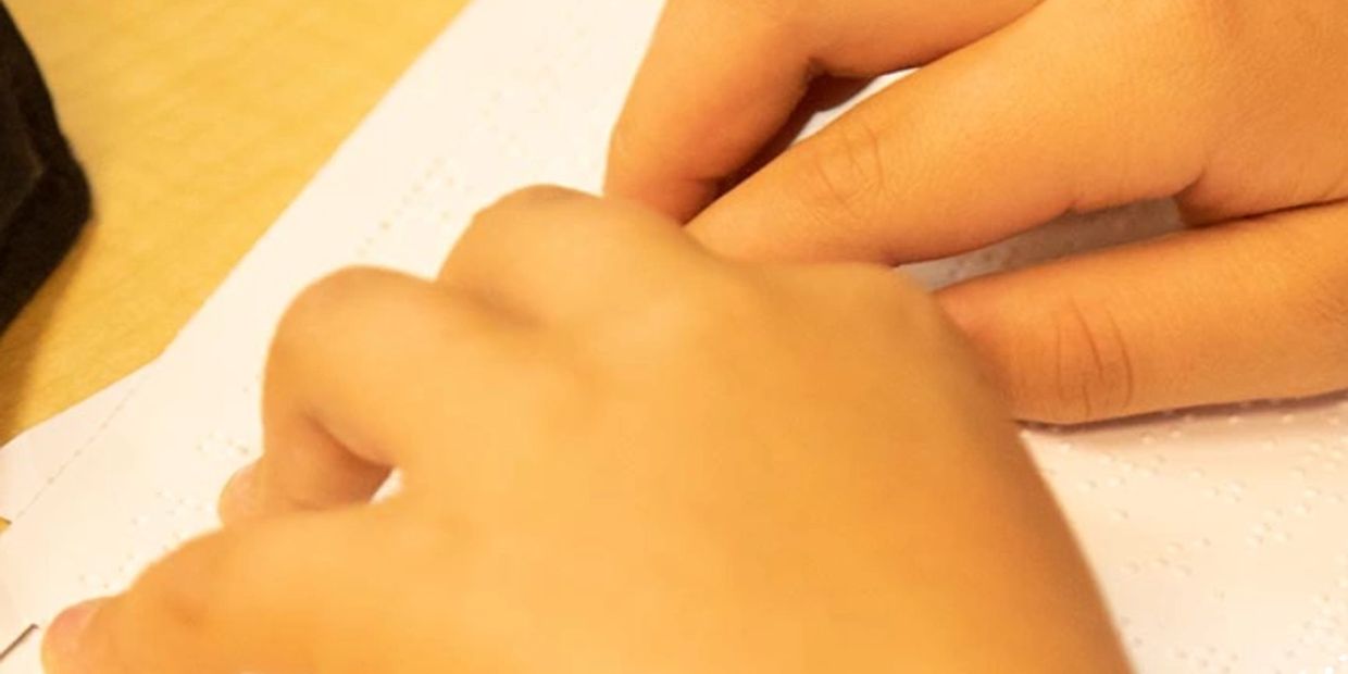 Students hand reading a braille book.