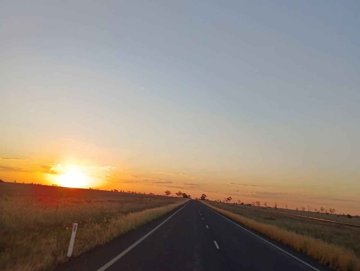 Empty road stretching into sunset with clear sky.
