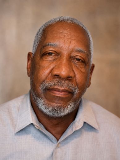 Portrait of an elderly man with gray hair and beard wearing a light blue shirt.