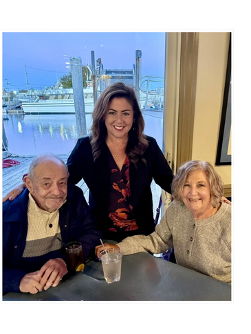 Three people smiling at a table near a marina.