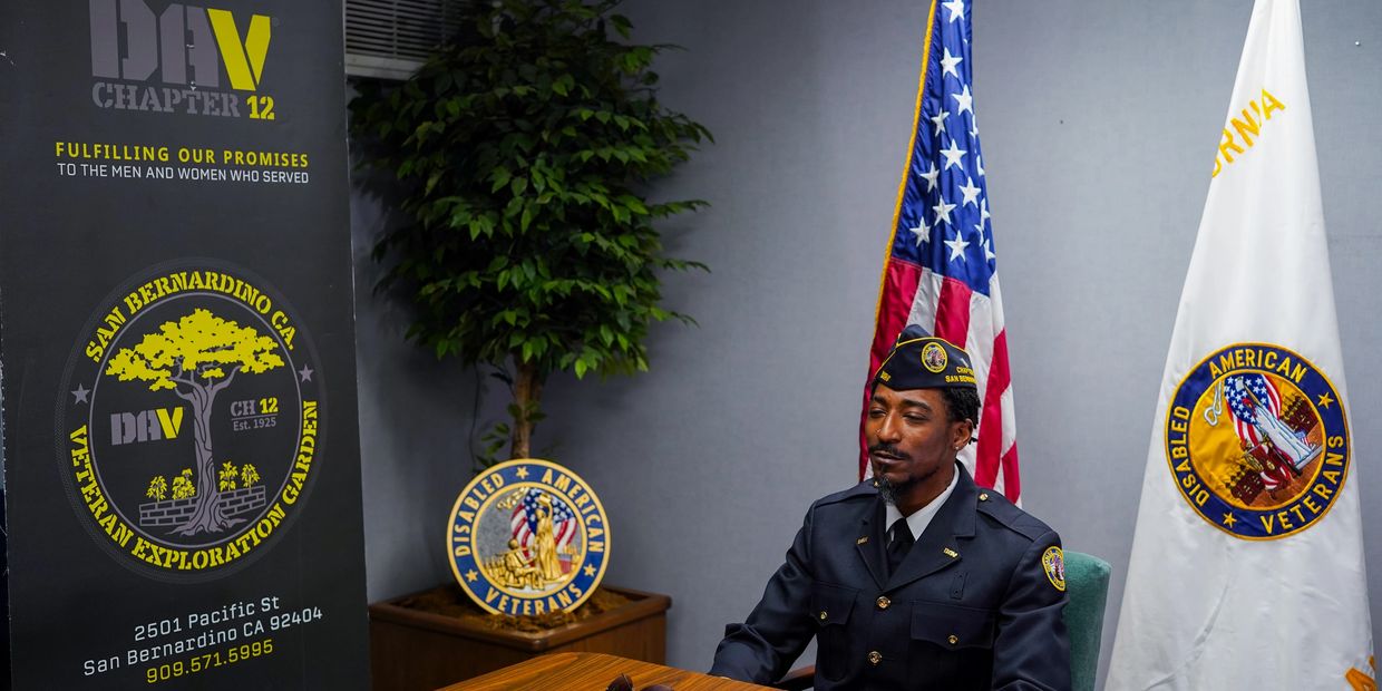 Veteran in uniform sits at table with American and Disabled American Veterans flags.