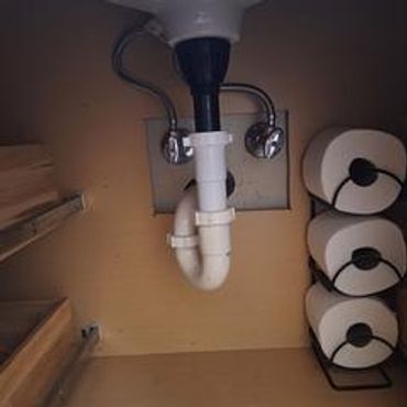 Under-sink plumbing with stacked toilet paper rolls beside it.